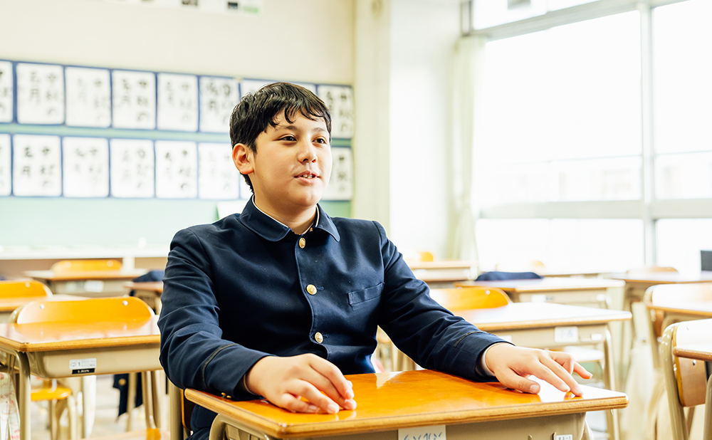 小学校の教室内でインタビューに答えるアレックスさん
