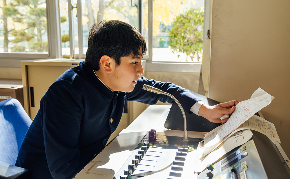 放送室で、校内放送を読み上げるアレックスさん